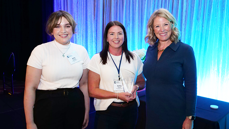 a photo showing three women in professional clothing standing in front of a teal-colored backdrop